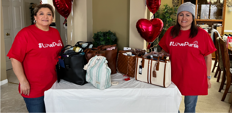Teresa L. and Nicole S. standing at the corner of a table filled with purses for #lovePurse campaign